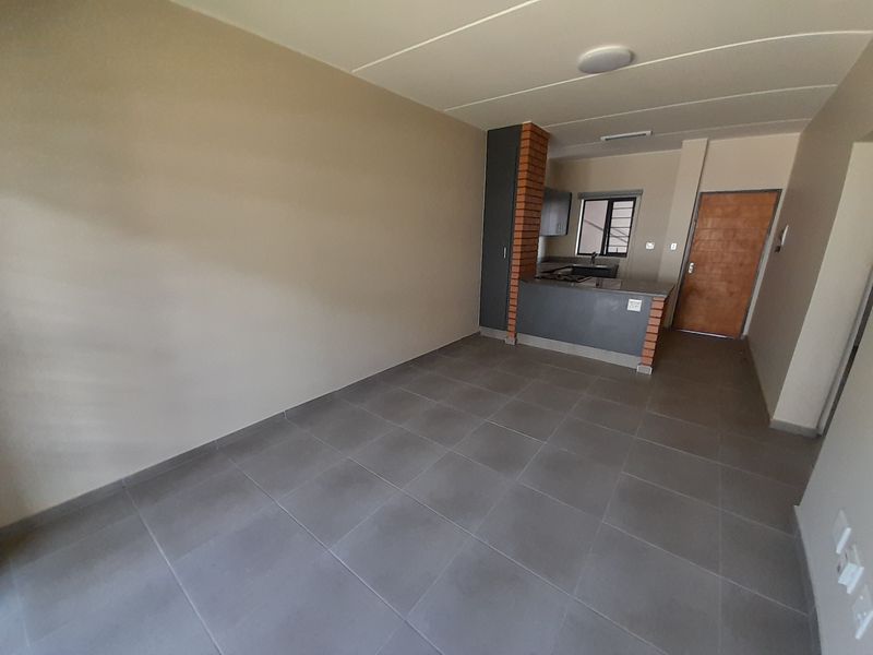 An open-plan living and kitchen area featuring neutral wall tones, grey floor tiles, and a functional kitchen layout with a breakfast counter.
