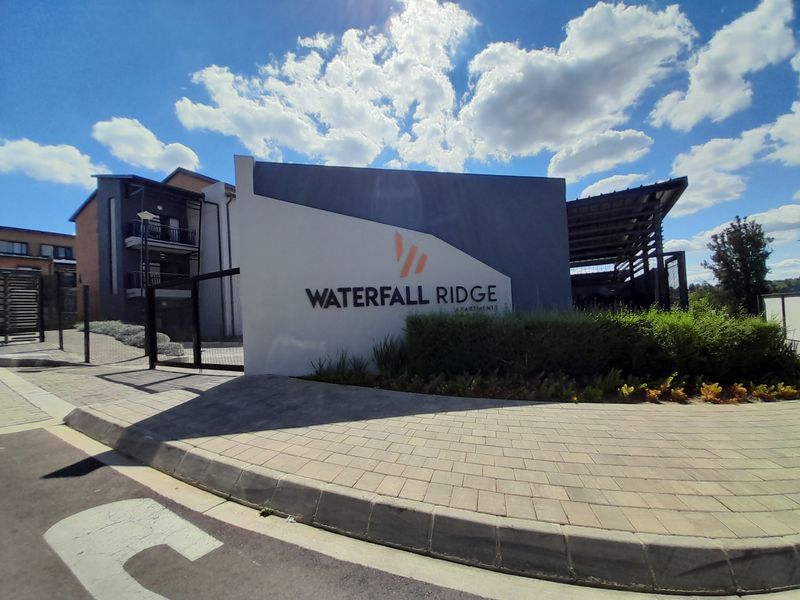 The entrance to Waterfall Ridge Apartments, featuring a modern complex sign, paved driveway, and secure gated access.