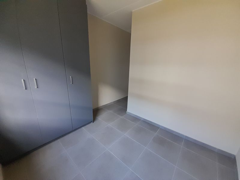 A clean, empty bedroom featuring neutral wall paint, grey tiled flooring, and modern built-in cupboards.