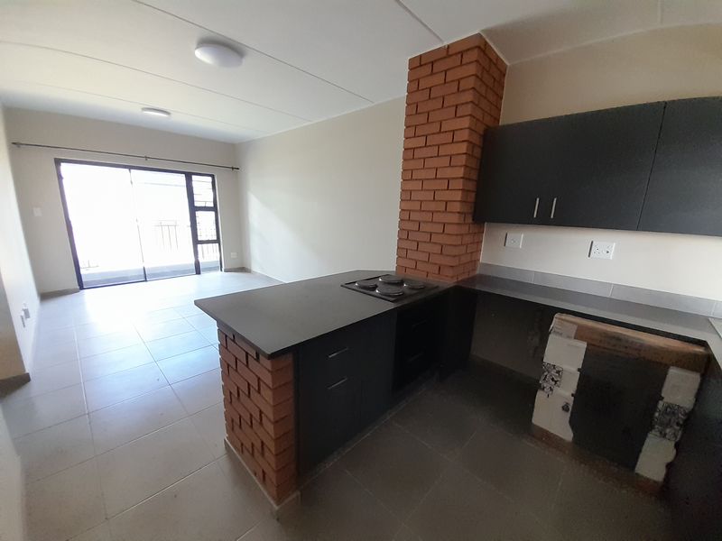 Open plan kitchen and living area featuring exposed brick accents, dark cabinetry, built-in hob and oven, and access to a balcony via sliding doors.