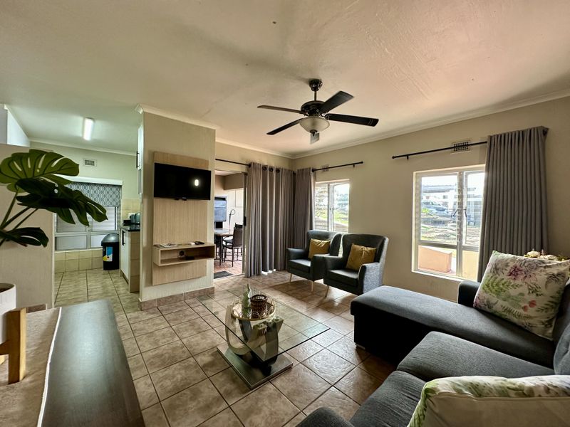 Open-plan living area featuring tiled flooring, a ceiling fan, and a built-in media unit, with direct access to an outdoor patio space.