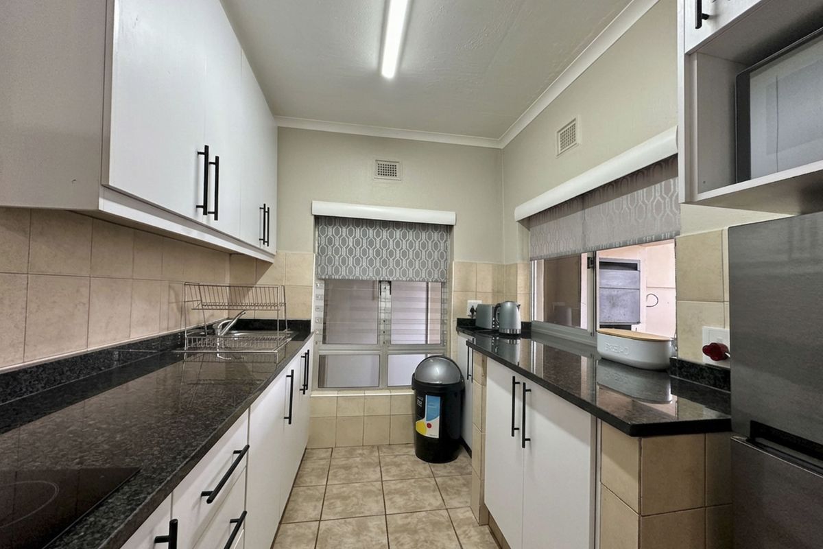 A functional galley-style kitchen featuring granite countertops, ample built-in cabinetry, tiled backsplash, and ceramic flooring with a pass-through window.