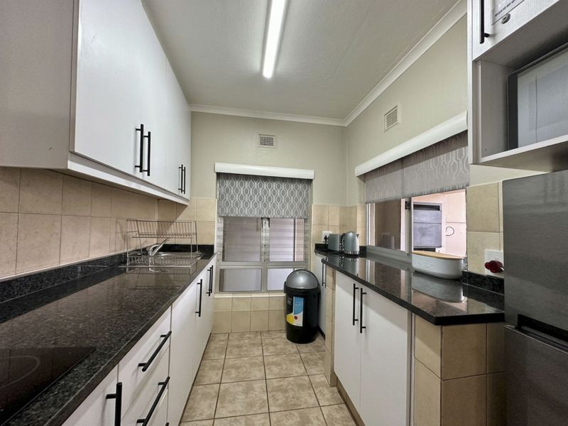 A functional galley-style kitchen featuring granite countertops, ample built-in cabinetry, tiled backsplash, and ceramic flooring with a pass-through window.