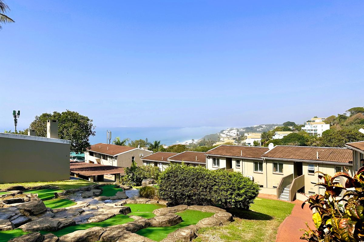A well-maintained communal garden area featuring a miniature golf course, paved walkways, and views of the surrounding residential complex and coastline.