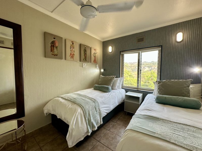 A compact bedroom featuring tiled flooring, a ceiling fan, and a window with natural light, finished with textured wall treatments.
