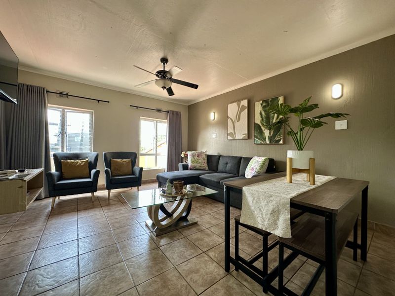 A well-maintained living room featuring tiled flooring, a ceiling fan, and wall-mounted lighting, offering a comfortable and functional space.