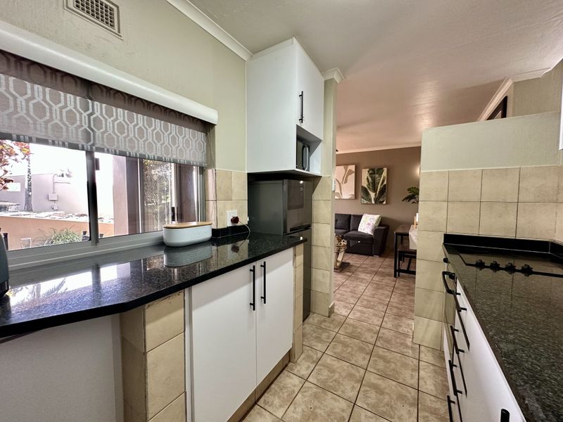 Functional kitchen featuring granite countertops, white cabinetry, and tiled flooring, with an open-plan layout flowing into the adjacent living area.