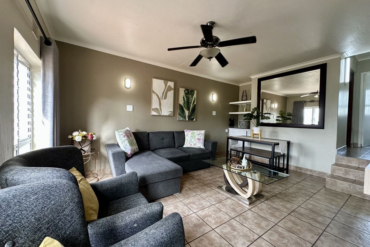 A comfortable living room featuring tiled flooring, a ceiling fan, wall sconces, and built-in shelving, creating a functional and inviting space.