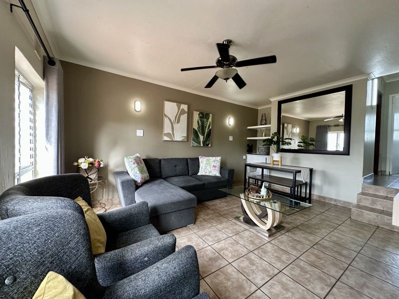 A comfortable living room featuring tiled flooring, a ceiling fan, wall sconces, and built-in shelving, creating a functional and inviting space.