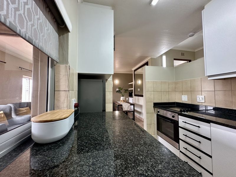 A functional kitchen featuring dark granite countertops, white cabinetry, a built-in oven, and an electric hob with a tiled backsplash.