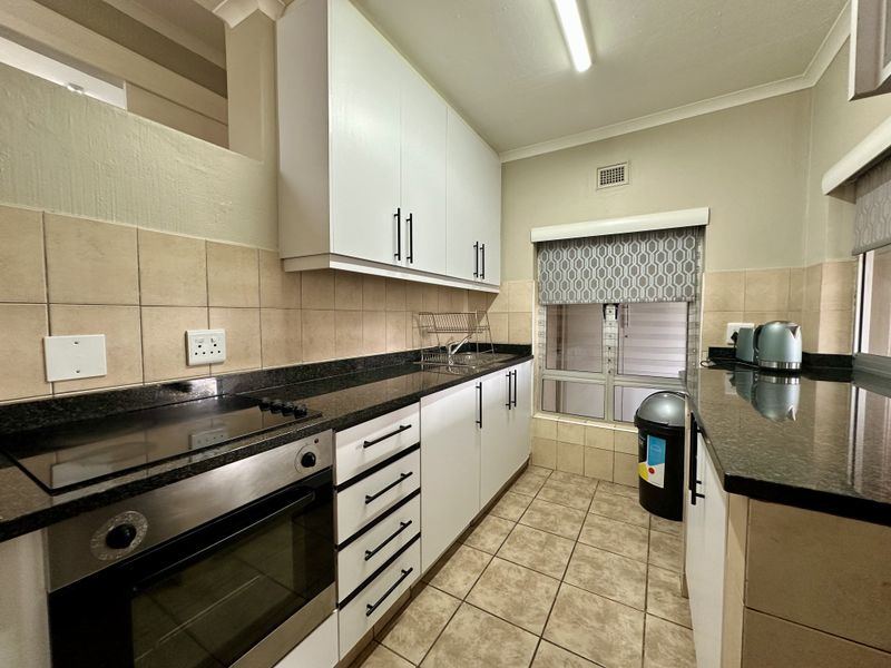 A functional kitchen featuring white cabinetry, dark granite countertops, a built-in oven, electric hob, and tiled flooring with a neutral backsplash.