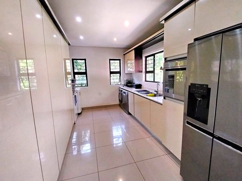 Modern kitchen featuring high-gloss cabinetry, integrated oven, stainless steel sink, and tiled flooring with ample natural light.