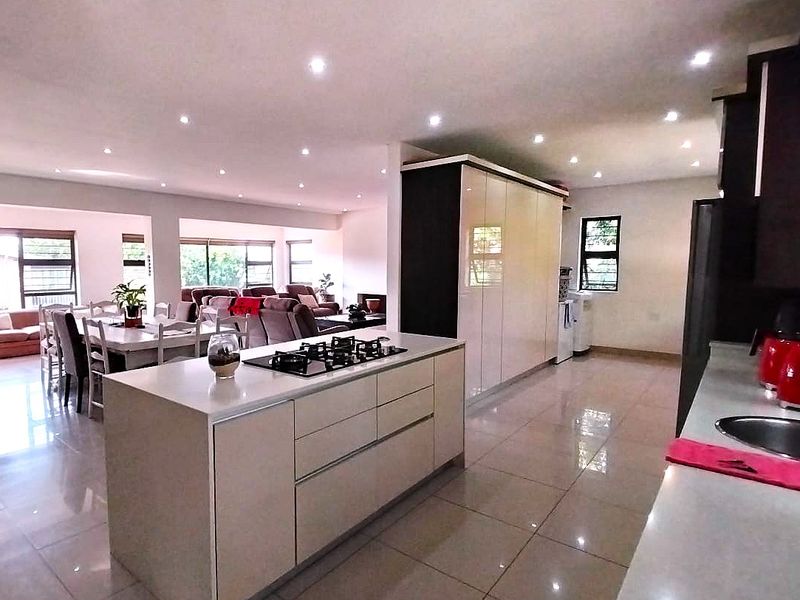 Spacious open-plan kitchen and living area featuring a central island with a gas hob, modern cabinetry, and polished tiled flooring throughout.
