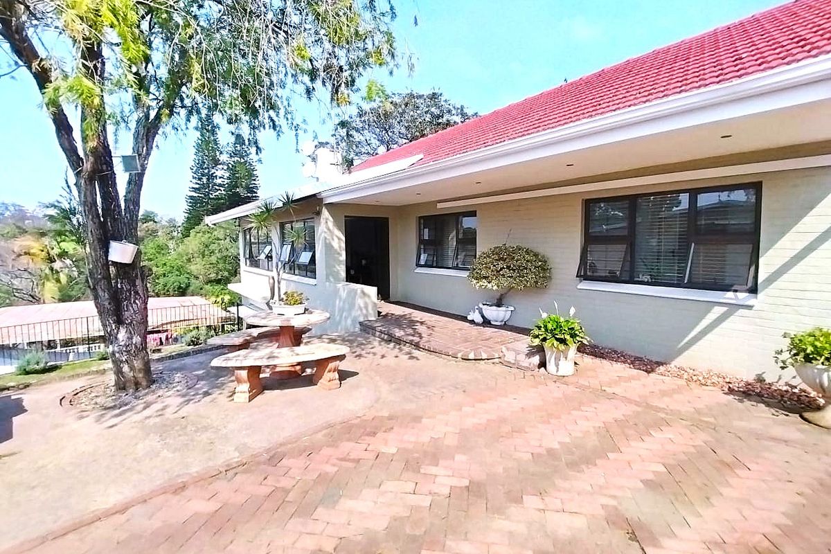 A rear exterior view of the house featuring a brick-paved patio area, tiled roof, and aluminium-framed windows overlooking the garden.
