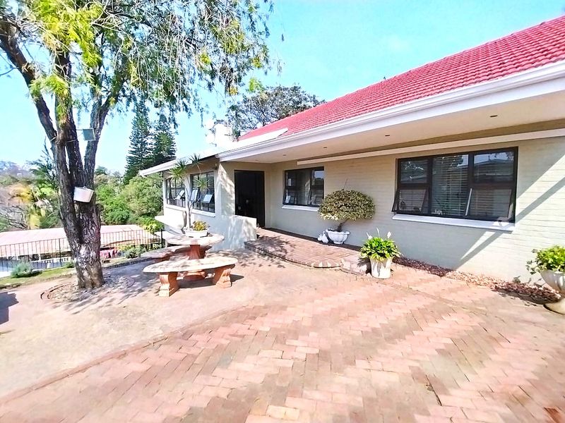 A rear exterior view of the house featuring a brick-paved patio area, tiled roof, and aluminium-framed windows overlooking the garden.