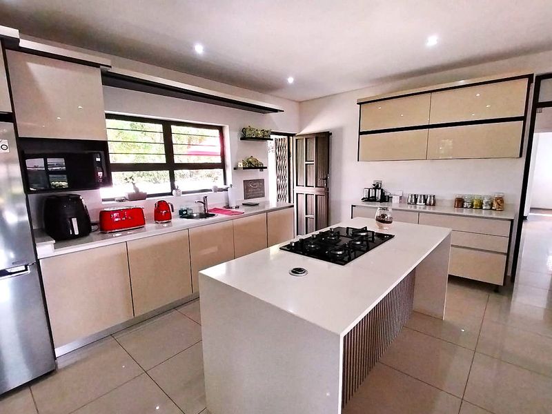 Modern kitchen featuring a central island with a gas cooktop, sleek cabinetry, stone countertops, and high-quality tiled flooring.