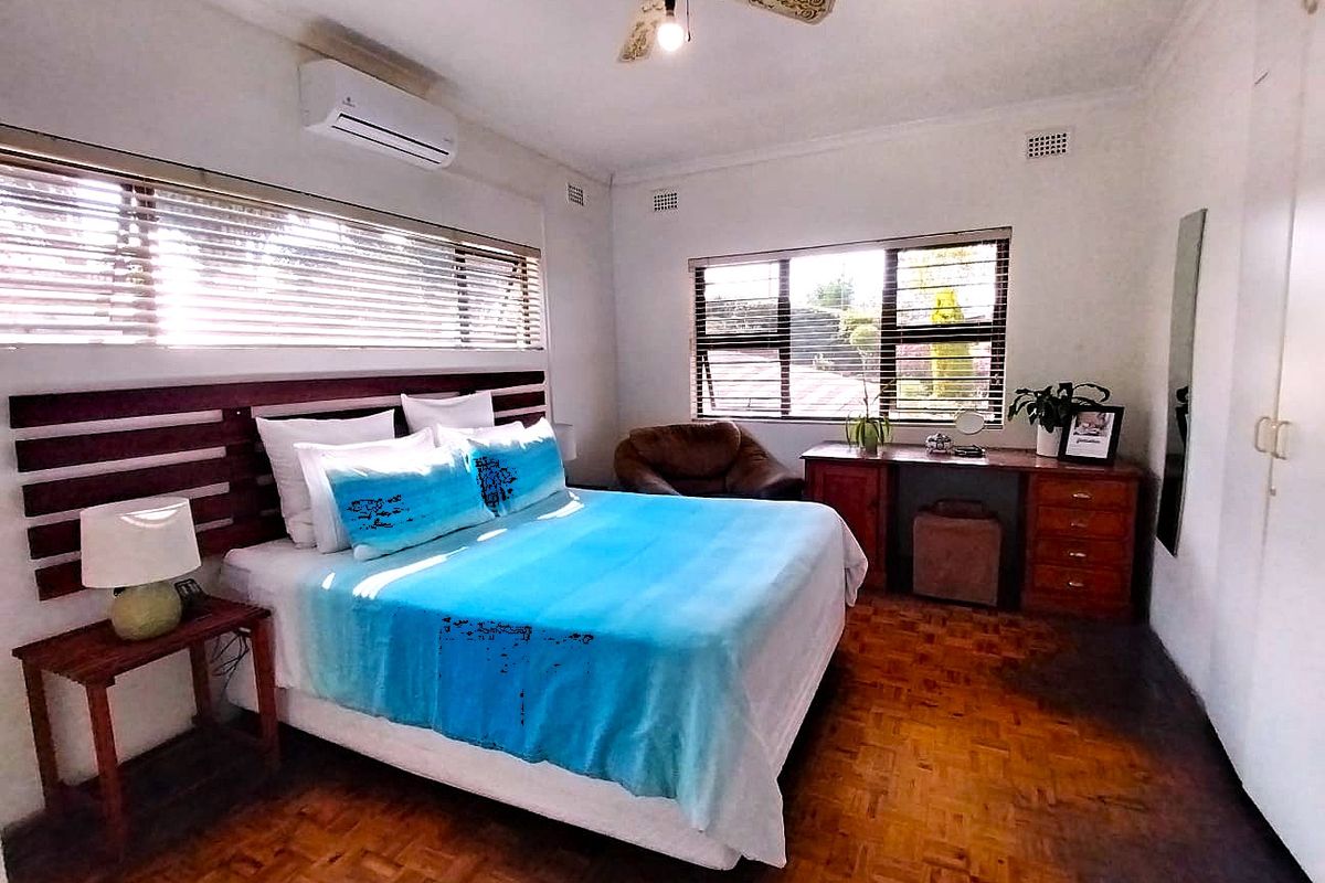 A spacious bedroom featuring parquet flooring, a ceiling fan, a split-system air conditioner, and built-in cupboards with large windows and venetian blinds.