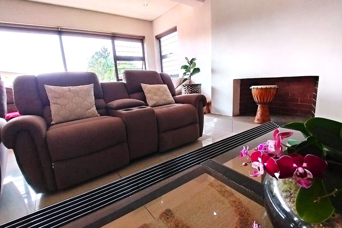 A bright living room featuring a built-in brick fireplace, large windows with aluminium frames, and neutral tiled flooring.