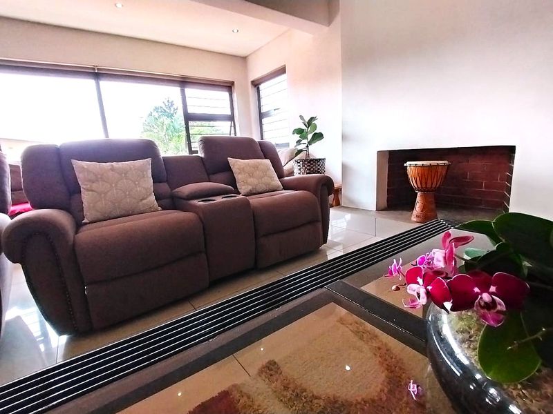 A bright living room featuring a built-in brick fireplace, large windows with aluminium frames, and neutral tiled flooring.