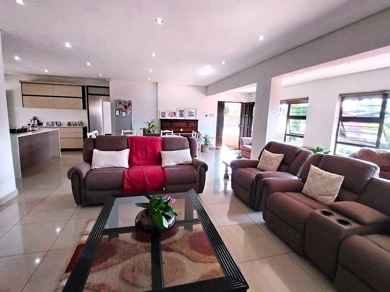 Spacious open-plan living area featuring tiled floors, recessed lighting, and a modern kitchen with a central island, flowing seamlessly to the outdoor space.
