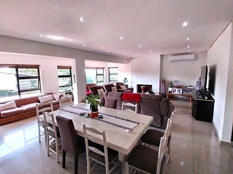 Spacious open-plan living and dining area featuring tiled floors, recessed downlighting, a built-in fireplace, and a wall-mounted air conditioning unit.