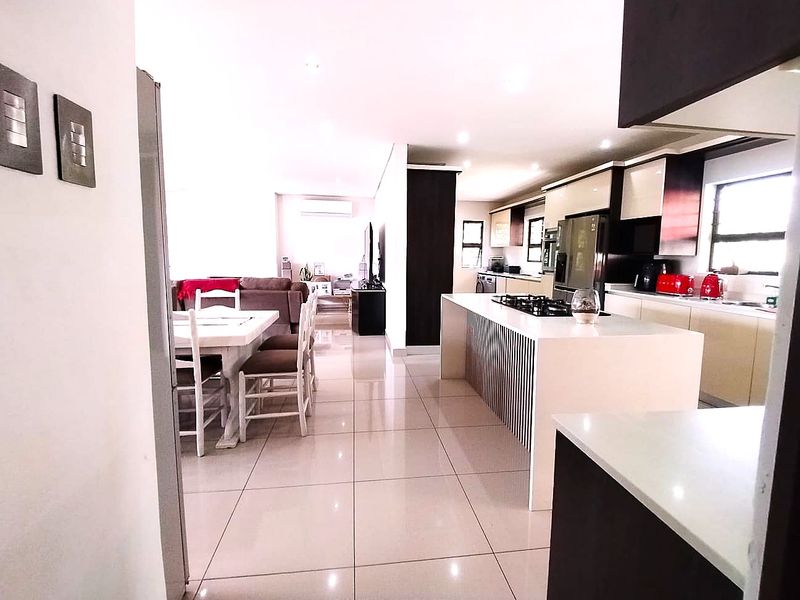 Modern open-plan living area featuring a sleek kitchen with a central island, gas hob, and high-gloss cabinetry, seamlessly flowing into the dining and lounge space.