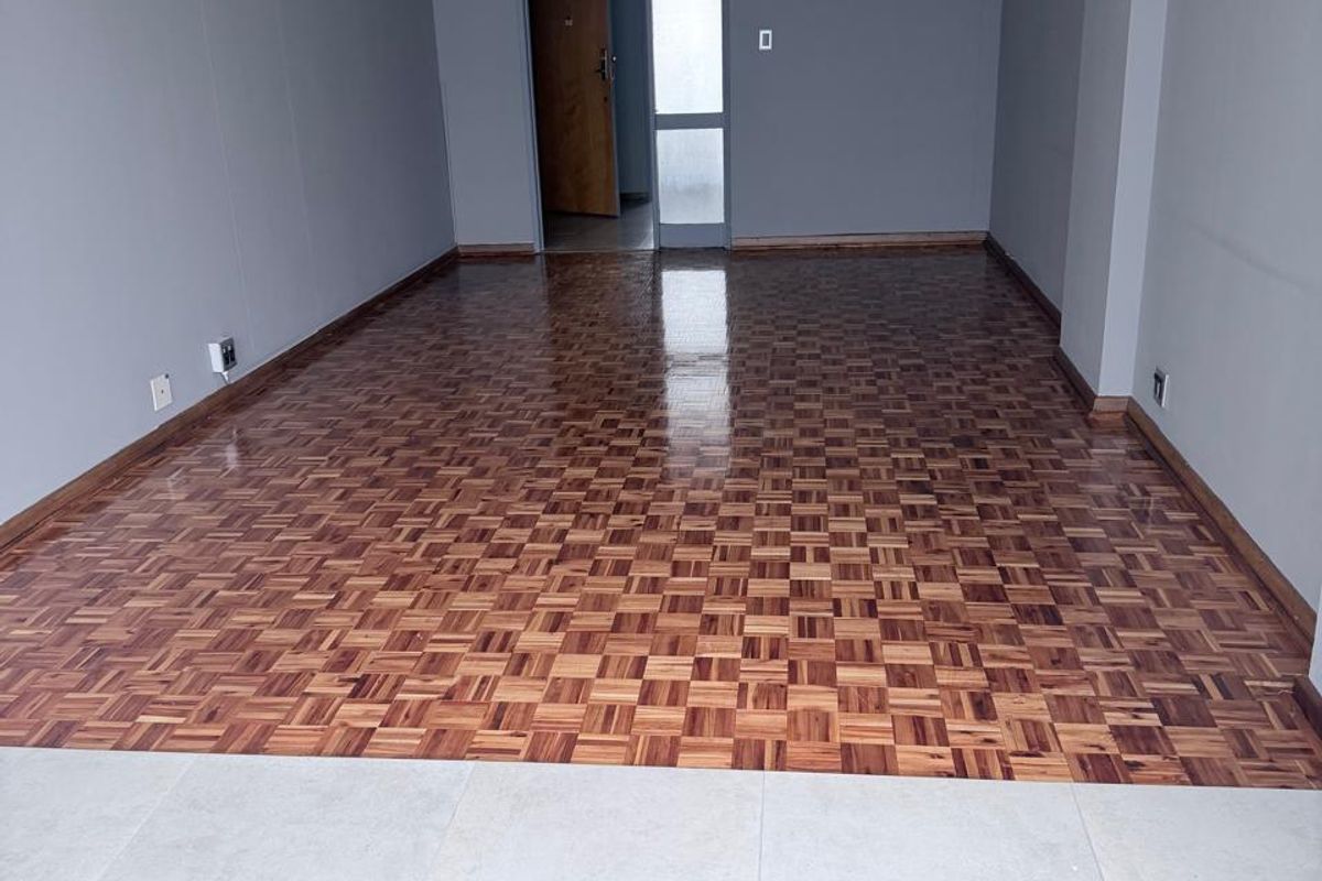 Spacious, empty living area featuring polished parquet flooring, neutral grey walls, and a modern pendant light fixture.