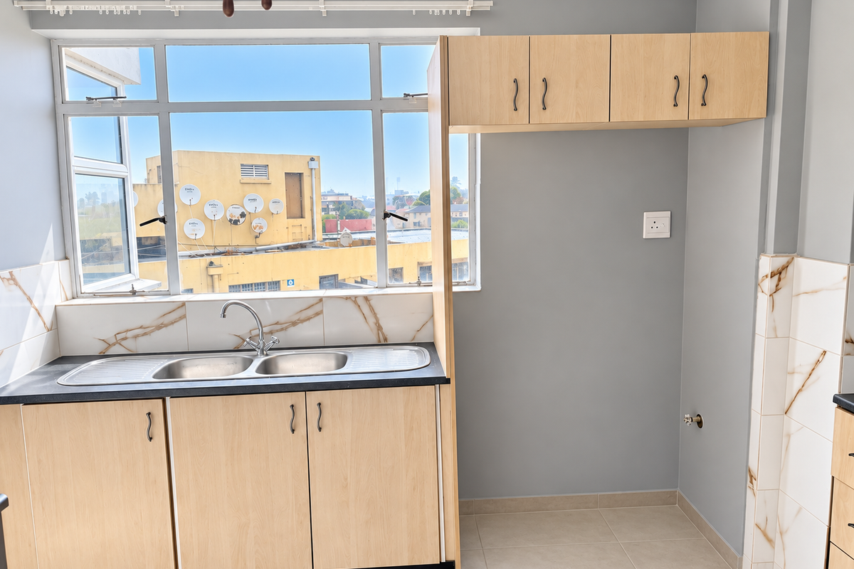 A clean, modern kitchen area featuring light wood cabinetry, a double stainless steel sink, and marble-look tiled splashbacks with ample natural light.