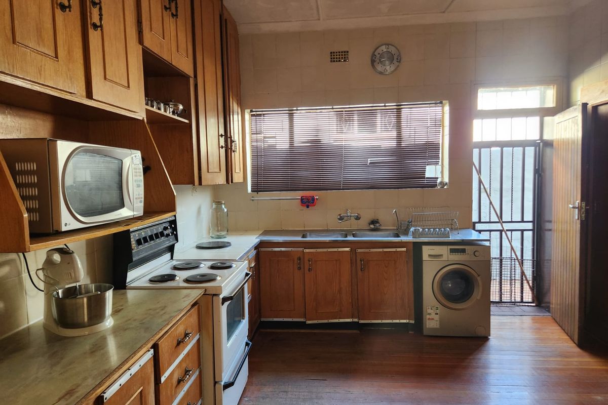 A functional kitchen featuring wooden cabinetry, a double basin sink, electric stove, and direct access to an exterior area through a security gate.