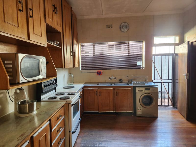 A functional kitchen featuring wooden cabinetry, a double basin sink, electric stove, and direct access to an exterior area through a security gate.