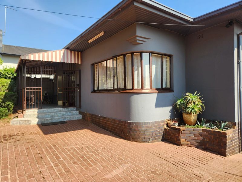 Front exterior view of the house featuring a brick paved driveway, a curved bay window, and a covered entrance area with security gates.