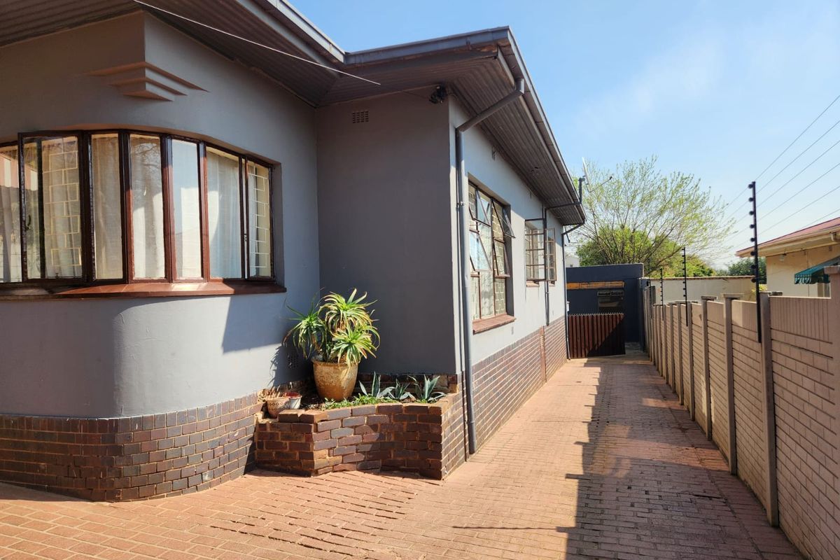 Side view of the property featuring brick paving, a built-in brick planter box, and secure perimeter walling with electric fencing.