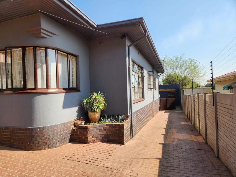 Side view of the property featuring brick paving, a built-in brick planter box, and secure perimeter walling with electric fencing.