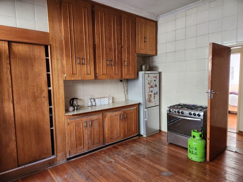 A dated kitchen featuring wooden cabinetry, tiled backsplash, and hardwood flooring, offering significant potential for a modern renovation.