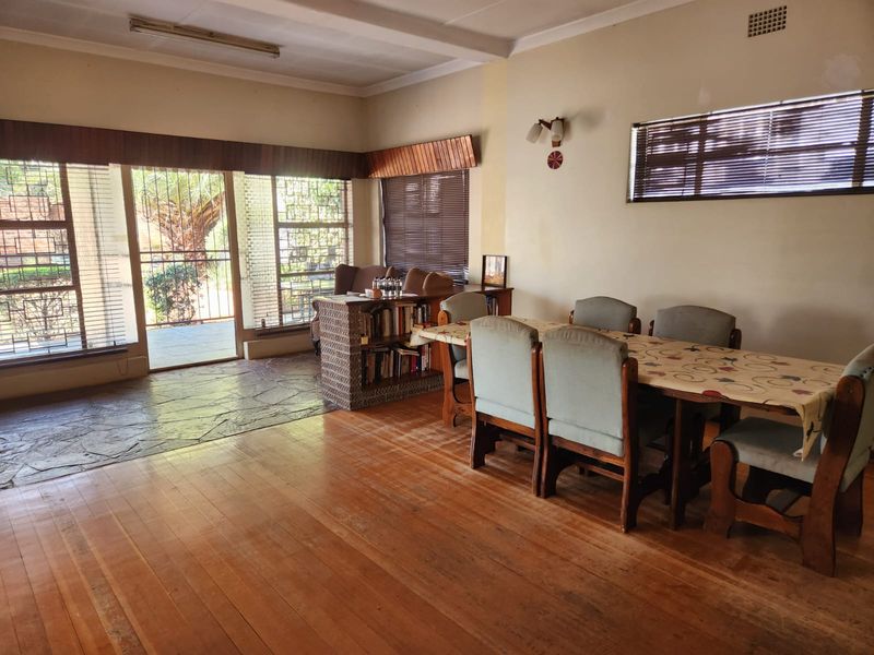Dining area featuring a combination of timber and stone flooring, large windows with venetian blinds, and direct access to the exterior via a security gate.
