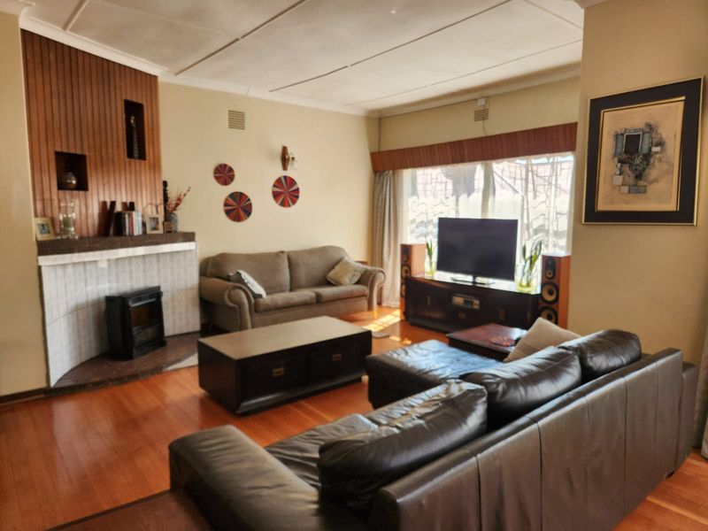 Spacious living room featuring hardwood flooring, a fireplace with timber paneling, and large windows allowing for natural light.