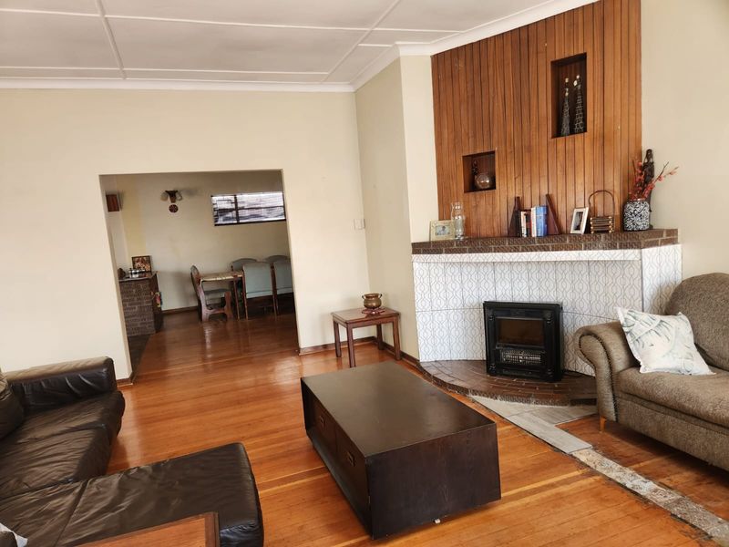 Spacious living room featuring hardwood flooring, a prominent tiled fireplace with wood paneling, and an open-plan flow into the adjacent dining area.