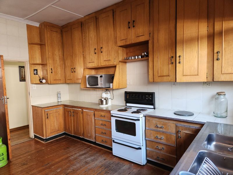 A functional kitchen featuring traditional wooden cabinetry, tiled backsplash, electric stove, and double basin sink, offering a classic layout with potential for modernization.