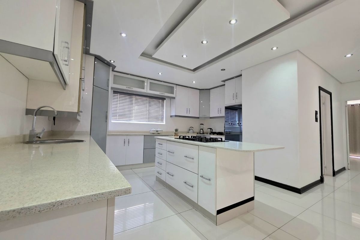 Modern, well-maintained kitchen featuring a central island with a gas cooktop, stone countertops, ample built-in cabinetry, and recessed ceiling lighting.