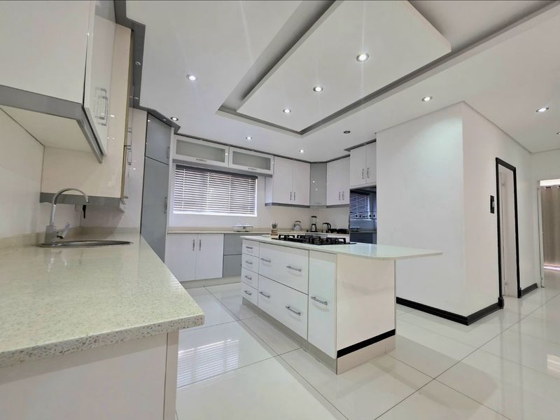 Modern, well-maintained kitchen featuring a central island with a gas cooktop, stone countertops, ample built-in cabinetry, and recessed ceiling lighting.