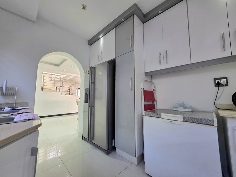 A functional scullery area featuring modern built-in cabinetry, stone countertops, a stainless steel sink, and space for a large refrigerator.
