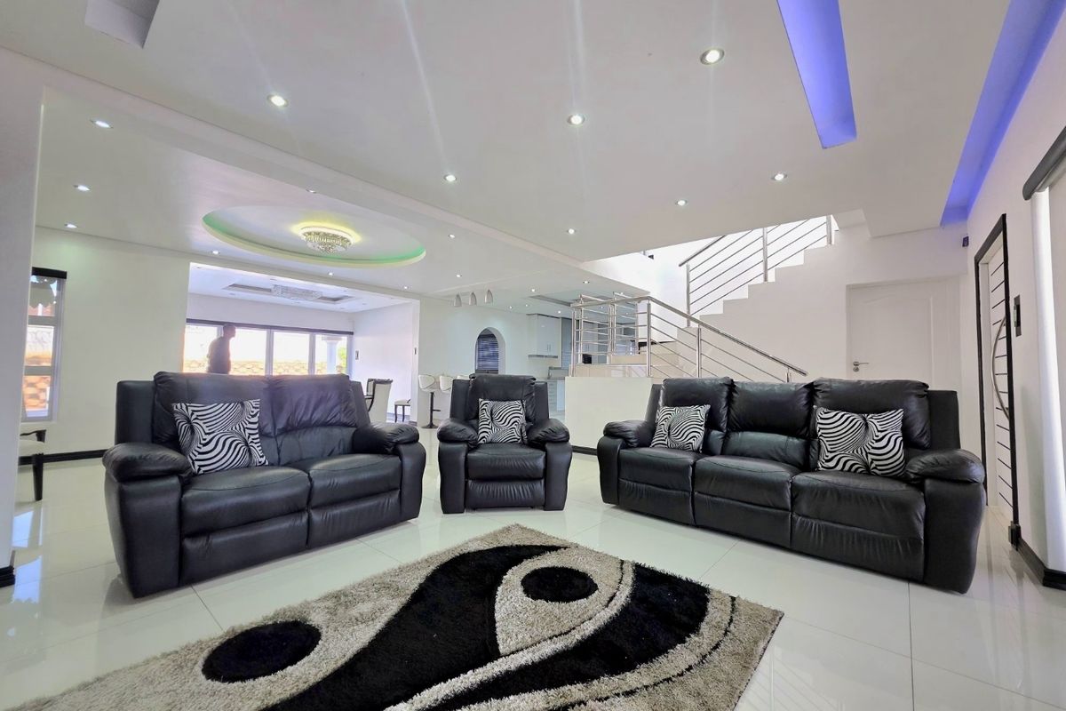 Spacious open-plan living area featuring modern recessed ceiling lighting, cove lighting, and a contemporary staircase with a metal balustrade.