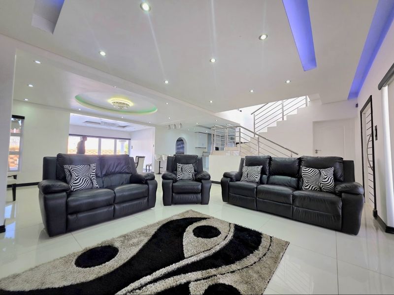 Spacious open-plan living area featuring modern recessed ceiling lighting, cove lighting, and a contemporary staircase with a metal balustrade.