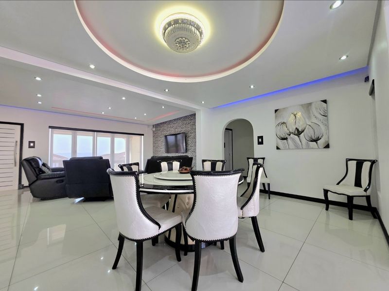 Spacious open-plan living and dining area featuring a modern coffered ceiling with ambient lighting, polished porcelain tiles, and a stone-clad feature wall.