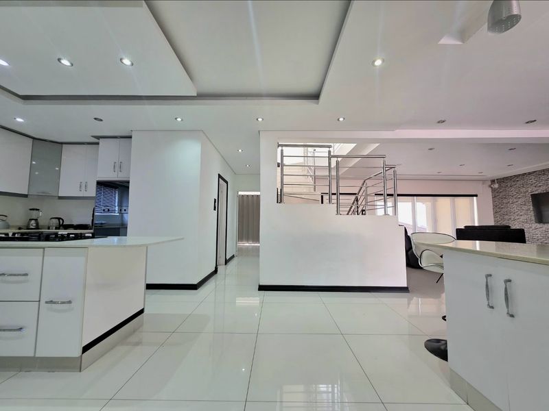 Modern open-plan living area featuring a sleek kitchen with island, polished tile flooring, and a contemporary staircase with stainless steel balustrade.