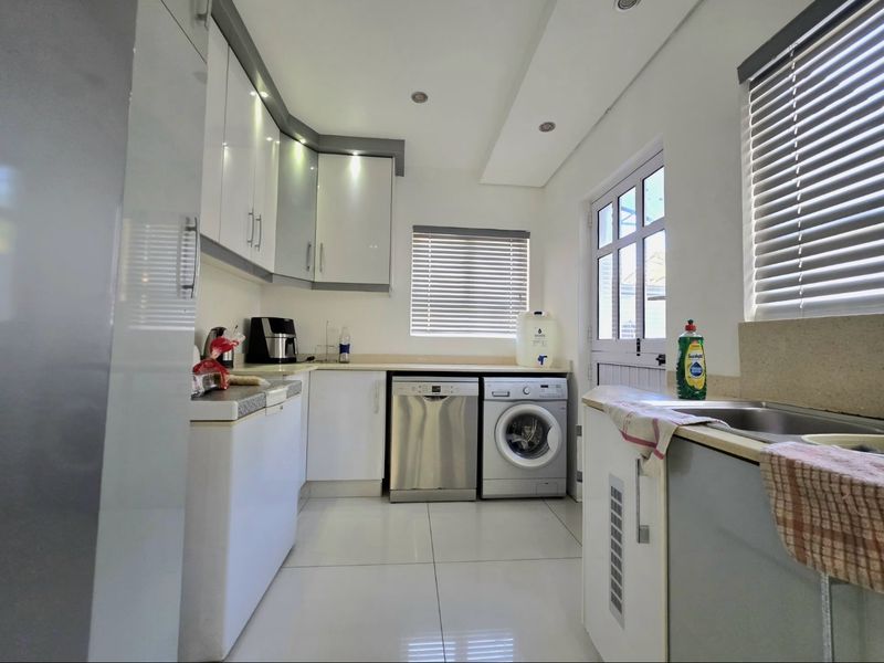 A clean and functional scullery featuring white cabinetry, stone countertops, integrated dishwasher, washing machine, and direct access to the exterior.