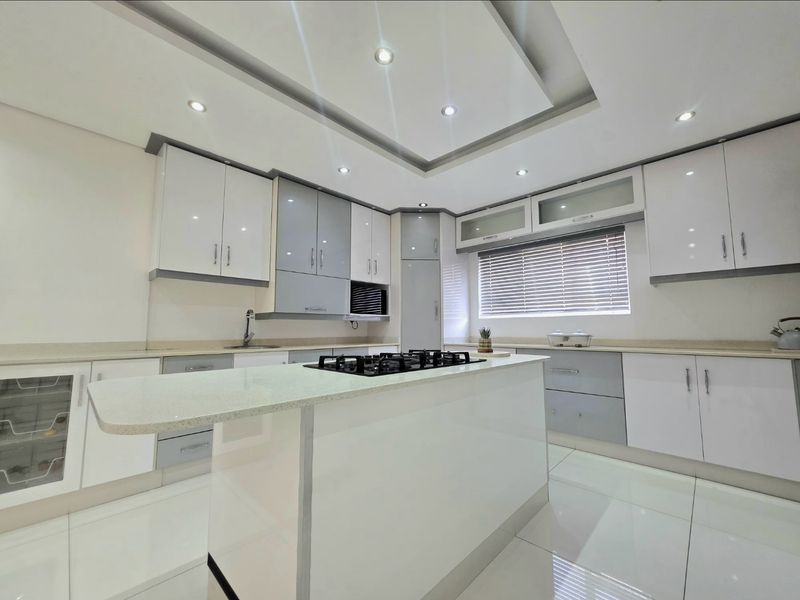 Modern kitchen featuring high-gloss cabinetry, a central island with a gas hob, stone countertops, and recessed ceiling lighting.