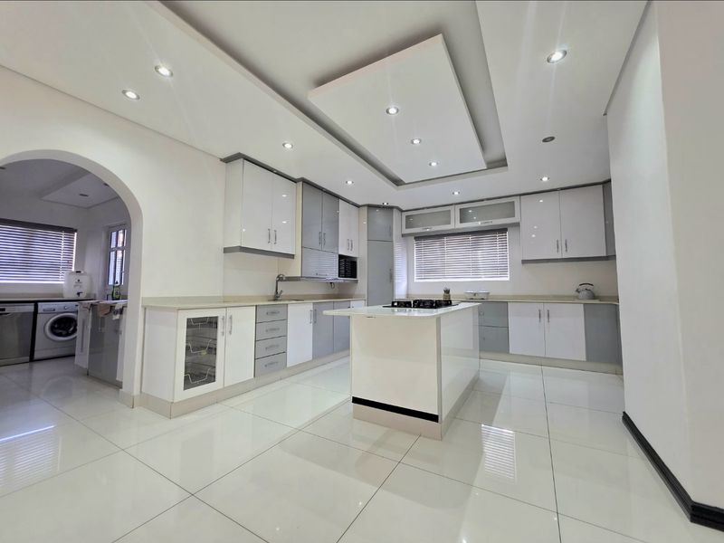 Modern kitchen featuring a central island with a gas cooktop, sleek white and grey cabinetry, recessed ceiling lighting, and polished tiled flooring.