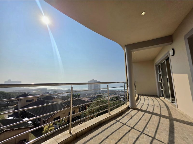 Spacious covered balcony featuring tiled flooring, a modern stainless steel balustrade, and expansive coastal views.