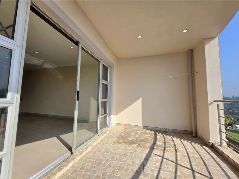A spacious covered balcony featuring tiled flooring, recessed lighting, and a stainless steel balustrade, accessible through large sliding glass doors.